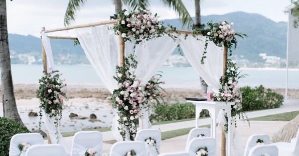 A wedding ceremony setup with white chairs and an arch with flowers. There is a body of water and mountains in the background.