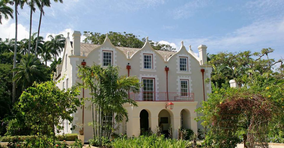 An elegant, cream-colored house with three stories situated between palm trees and foliage in the front yard's landscaping.