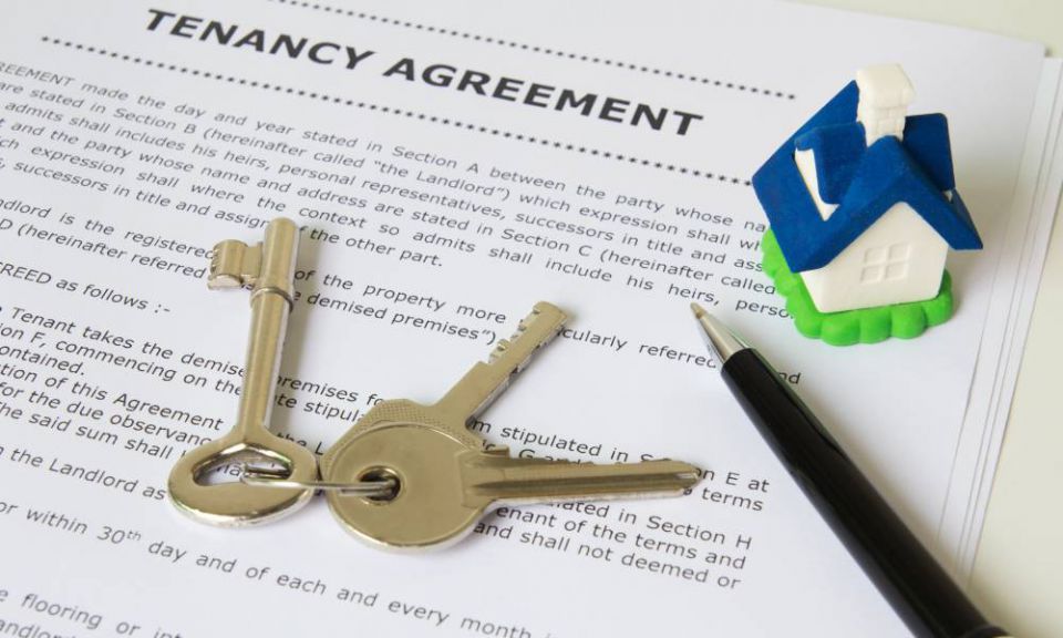 Close-up of a tenancy agreement with a pen, a pair of keys to the property, and a small house figurine on a table.